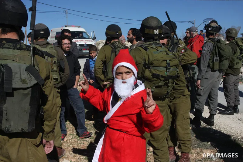 A young demonstrator dressed as Santa Claus stands near Israeli soldiers standing guard during a protest against the controversial Israeli barrier in the West Bank village of al-Masara near Bethlehem December 23, 2011. P...