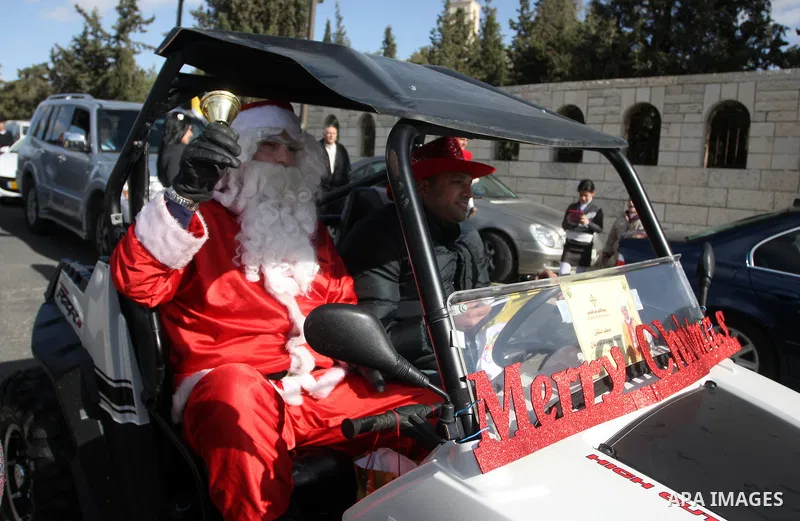 A man dressed as Father Christmas drives past the Israeli built separation barrier as Christians arrive to celebrate Christmas mass in the West Bank city of Bethlehem, on December 24, 2011. Photo by Issam Rimawi