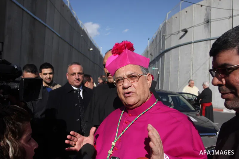 The Latin Patriarch of Jerusalem Fouad Twal (L) waves near the controversial Israeli barrier as he heads to the Church of the Nativity to attend Christmas celebrations in the West Bank town of Bethlehem December 24, 2011...