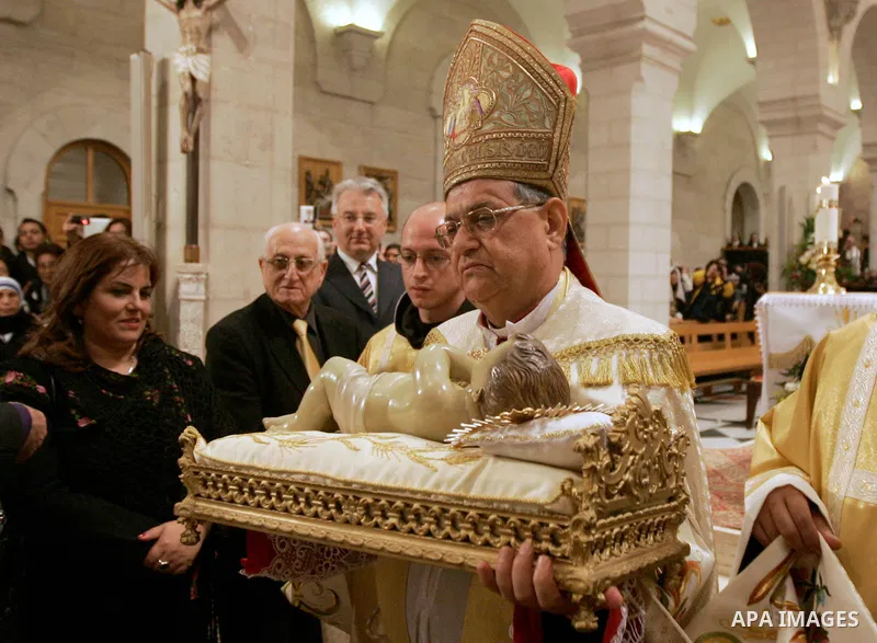 Latin Patriarch of Jerusalem Fouad Twal carries the statuette of baby Jesus during the Christmas midnight Mass at the Church of the Nativity, traditionally believed to be the birthplace of Jesus Christ, in the West Bank...