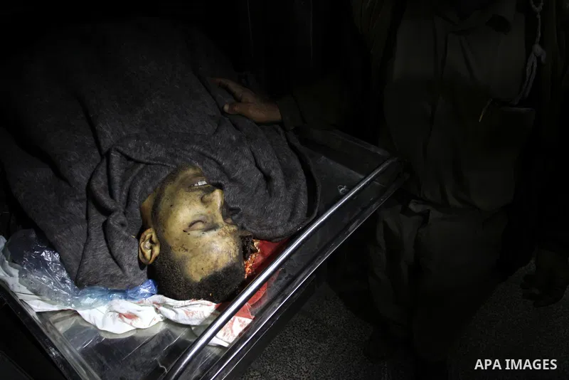 A man stands next to the body of a Palestinian killed in an explosion, apparently caused by an Israeli air strike, at a hospital in the northern Gaza Strip December 27, 2011. An explosion, apparently caused by an Israeli...