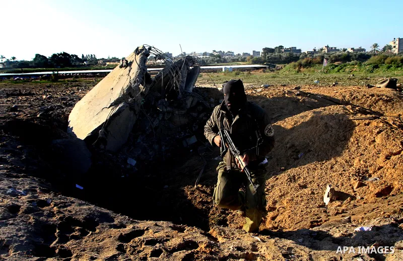 A masked Palestinian Islamic Jihad militant is seen through a tyre as he surveys the damage at a training camp after an Israeli air strike in Gaza December 29, 2011. The Israeli army confirmed that it targeted two sites...