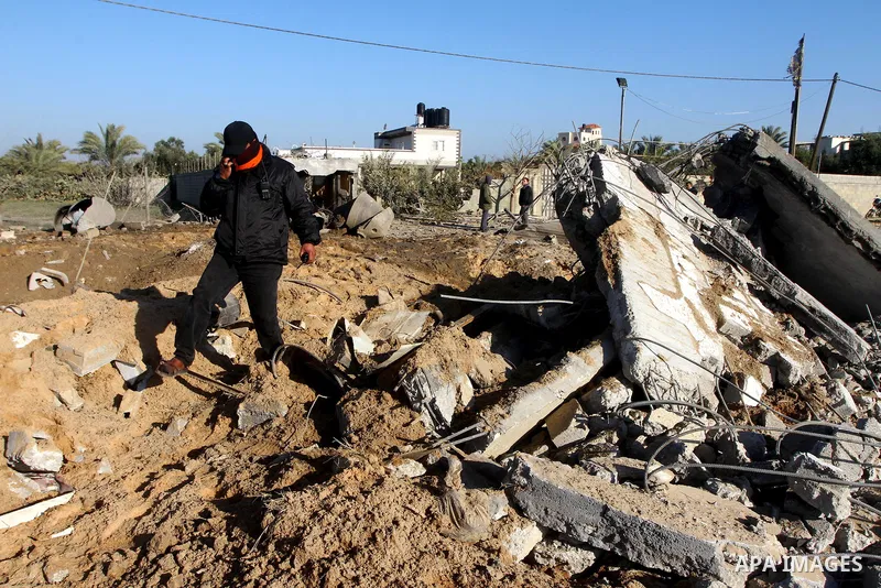 A masked Palestinian Islamic Jihad militant is seen through a tyre as he surveys the damage at a training camp after an Israeli air strike in Gaza December 29, 2011. The Israeli army confirmed that it targeted two sites...
