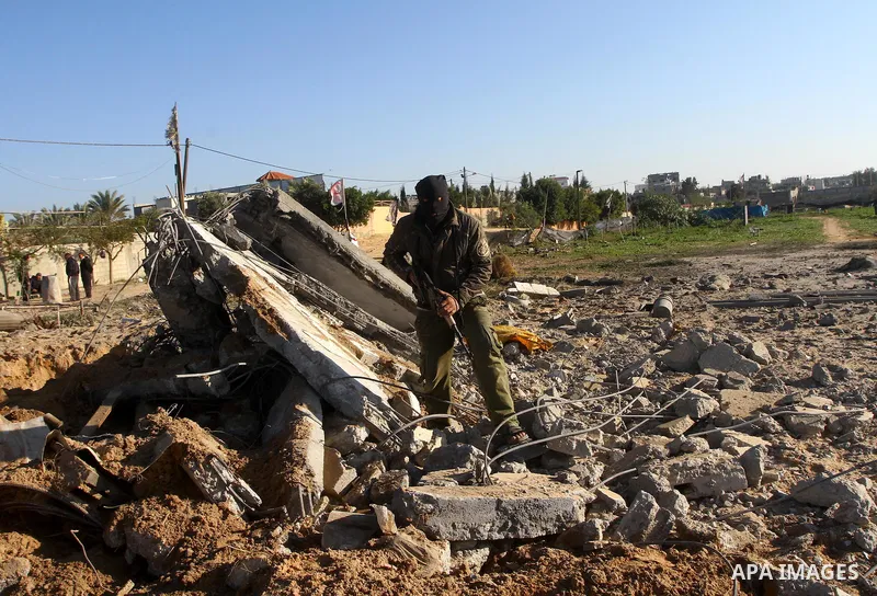 A masked Palestinian Islamic Jihad militant is seen through a tyre as he surveys the damage at a training camp after an Israeli air strike in Gaza December 29, 2011. The Israeli army confirmed that it targeted two sites...