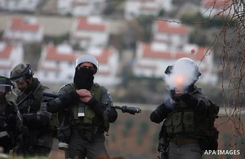 An Israeli soldier fires his weapon at Palestinian youths during demonstration against the expansion of the nearby Jewish settlement of Halamish in the West Bank village of Nabi Saleh near Ramallah, Friday, Dec. 30, 2011...