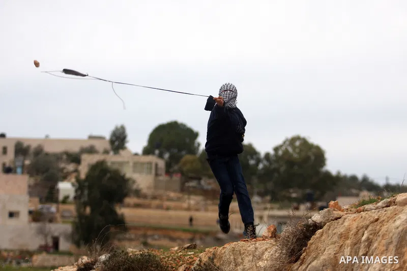 A Palestinian protester hurls stones at Israeli soldiers during demonstration against the expansion of the nearby Jewish settlement of Halamish in the West Bank village of Nabi Saleh near Ramallah, Friday, Dec. 30, 2011....