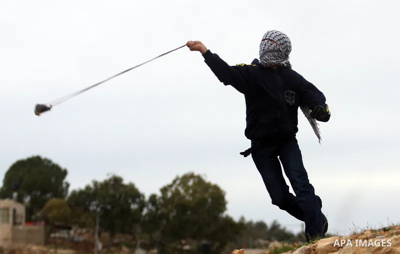 A Palestinian protester hurls stones at Israeli soldiers during demonstration against the expansion of the nearby Jewish settlement of Halamish in the West Bank village of Nabi Saleh near Ramallah, Friday, Dec. 30, 2011....