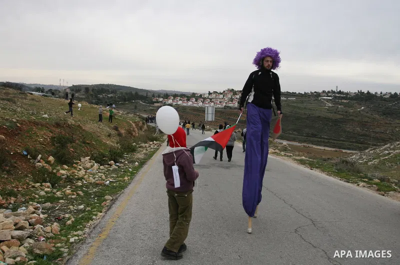 An activist walking on stilts holds a Palestinian flag during a weekly protest against a nearby Jewish settlement, in the West Bank village of Nabi Saleh, near Ramallah, December 30, 2011. Photo by Issam Rimawi