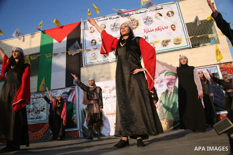 Palestinian folkloric dancers perform in front of a poster showing the late Palestinian leader Yasser Arafat during a celebration to to mark the 47th anniversary of the Fatah political movement. in the West Bank city of...