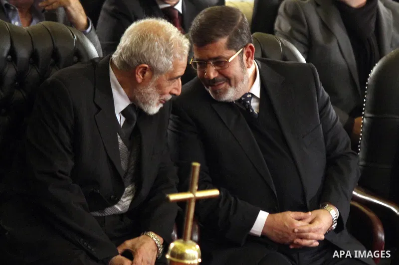 Mohamed Mursi (R), the head of the Muslim Brotherhood's Freedom and Justice Party, speaks with the Brotherhood's deputy leader Mohamed Ezzat during the Coptic Christmas eve mass at the main cathedral in Cairo January 6,...