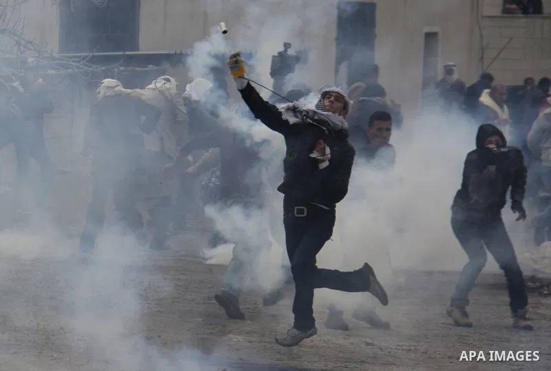 Palestinian protesters clash with Israeli troops as a tear gas canister flies overhead during a weekly protest against the Jewish settlement of Qadomem, near Nablus, the West Bank, 13 January 2012. Ten Palestinians and t...