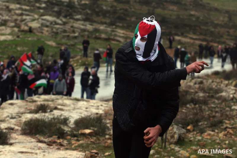 Palestinians wear balaclavas designed as their national flag and throw stones at Israeli soldiers during a protest against the expansion of the nearby Jewish settlement of Halamish in the West Bank village of Nabi Saleh...