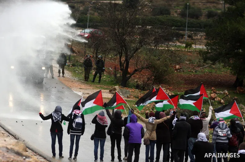 Palestinians wave flags in front of a truck spraying foul smelling water during clashes with stone-throwing demonstrators and Israeli soldiers at a weekly protest in the West Bank village of Nabi Saleh, near Ramallah Jan...