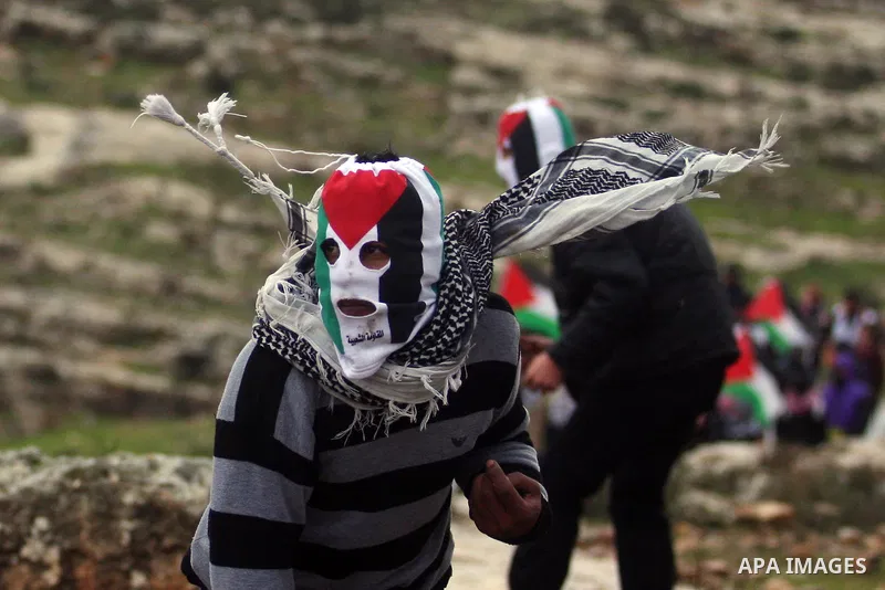 Palestinians wear balaclavas designed as their national flag and throw stones at Israeli soldiers during a protest against the expansion of the nearby Jewish settlement of Halamish in the West Bank village of Nabi Saleh...