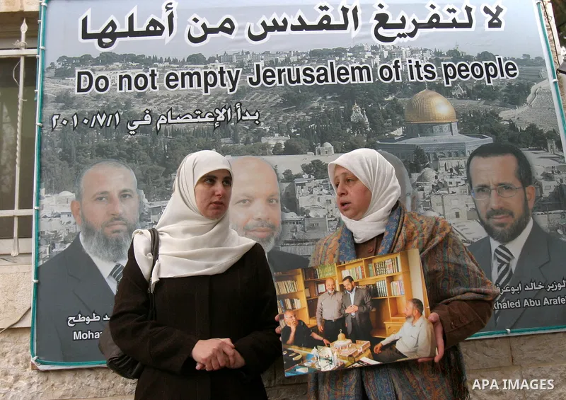 Palestinian women stand outside the Red Cross offices in east Jerusalem on January 23, 2012 in front of a poster bearing pictures of four senior Hamas officials whom Israel has been seeking to expel, sparking concern amo...