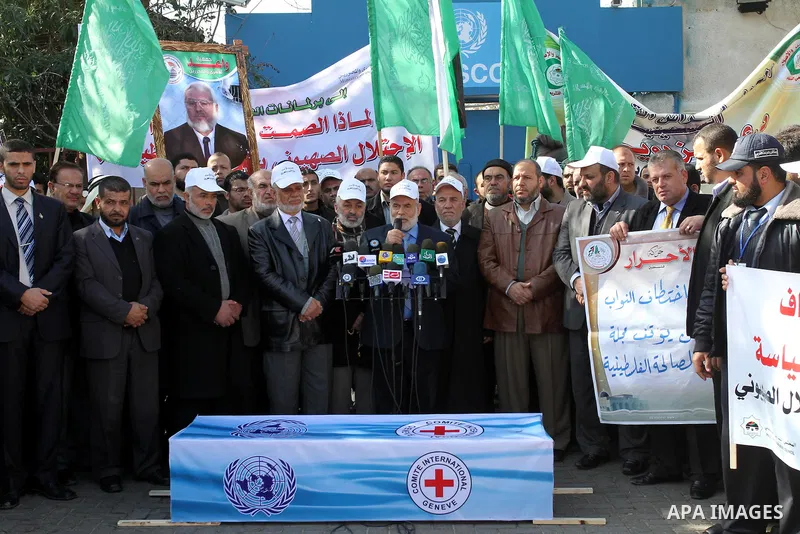 Palestinian Legislative Council members and other officials stand around a mock coffin covered with the emblems of the International Committee of the Red Cross (ICRC) and the United Nations Relief and Works Agency (UNRWA...