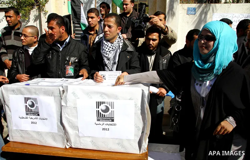 Palestinian activists wave Palestinian flags and hold election ballots during a protest calling for elections and unity between Fatah and Hamas during a demonstration in front of the recently reopened Central Elections c...