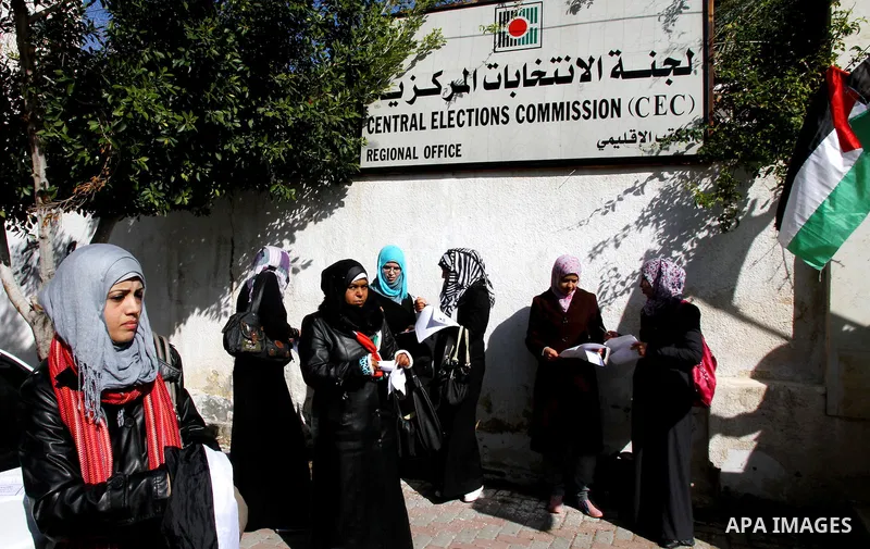 Palestinian activists wave Palestinian flags and hold election ballots during a protest calling for elections and unity between Fatah and Hamas during a demonstration in front of the recently reopened Central Elections c...