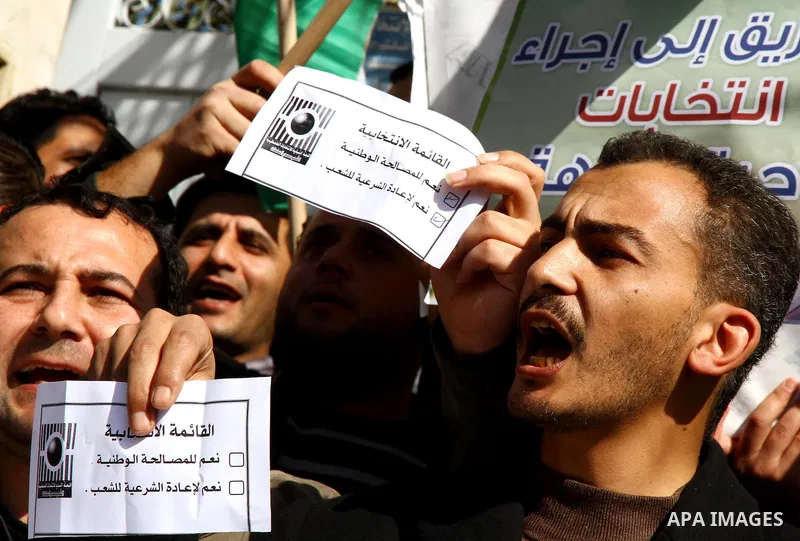 Palestinian activists wave Palestinian flags and hold election ballots during a protest calling for elections and unity between Fatah and Hamas during a demonstration in front of the recently reopened Central Elections c...