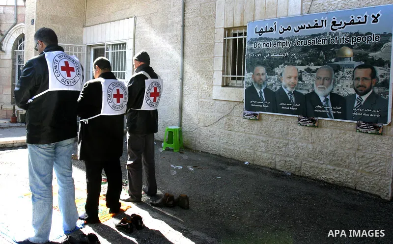 Red Cross staffers perform Friday prayers outside the organisation's offices in east Jerusalem on January 27, 2012 in front of a poster bearing pictures of four senior Hamas officials whom Israel has been seeking to expe...