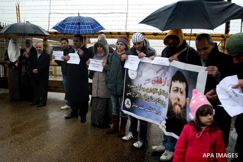 Maali (R), daughter of jailed Islamic Jihad spokesman Khodr Adnan (poster), stands with protesters holding signs against administrative detention during a demonstration outside Israel's Ofer prison near the West Bank tow...