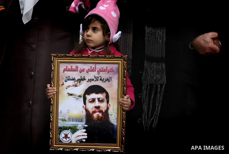 Maali, daughter of jailed Islamic Jihad spokesman Khodr Adnan (poster), stands with protesters holding signs against administrative detention during a demonstration outside Israel's Ofer prison near the West Bank town of...