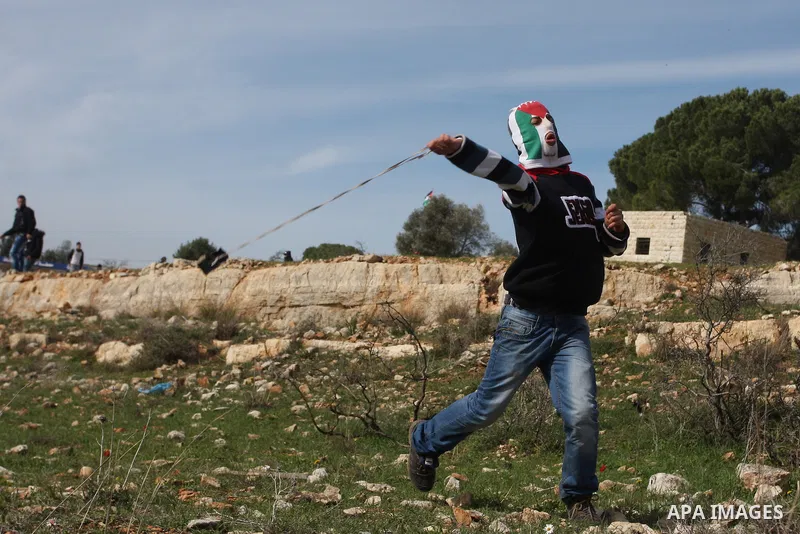 A Palestinian youth hurls stones at Israeli troops during a weekly protest against the construction of Israel's controversial separation barrier and the expansion of Jewish settlements in the West Bank village of Nabi Sa...