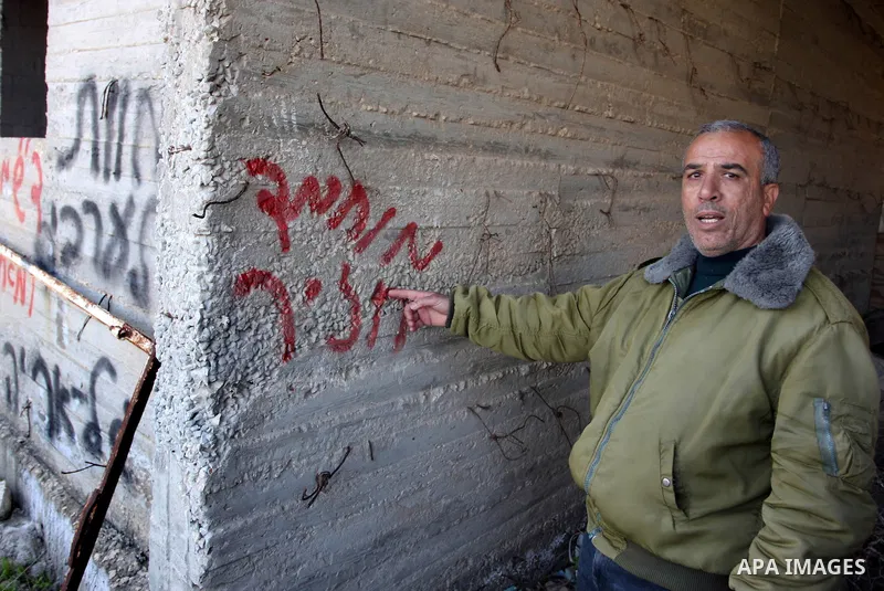 Palestinians look at graffiti sprayed on his house in the West Bank village of El-Jinya near Ramallah, Sunday, Feb. 5, 2012. Palestinians say extremist Jews have scrawled their home in a West Bank village with offensive...
