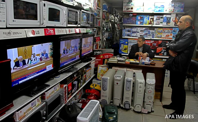 Palestinians watch at their shop as a television broadcasts the signing of a reconciliation agreement in Qatar between Hamas and Fatah, in Gaza city, Monday, Feb. 6, 2012. The main Palestinian political rivals on Monday...