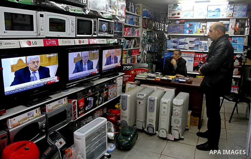 Palestinians watch at their shop as a television broadcasts the signing of a reconciliation agreement in Qatar between Hamas and Fatah, in Gaza city, Monday, Feb. 6, 2012. The main Palestinian political rivals on Monday...
