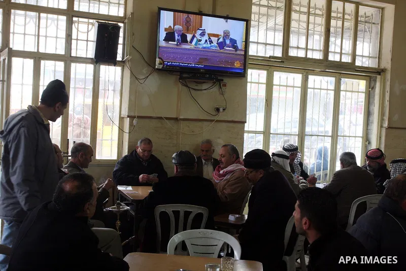 Palestinians play cards at a coffee shop as a television broadcasts the signing of a reconciliation agreement in Qatar between Hamas and Fatah, in the West Bank city of Ramallah, Monday, Feb. 6, 2012. The main Palestinia...