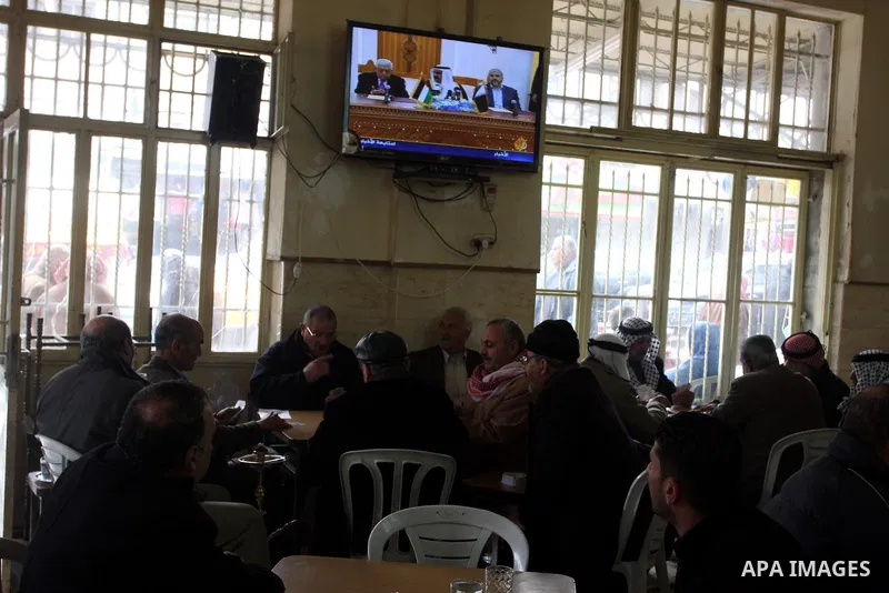 Palestinians play cards at a coffee shop as a television broadcasts the signing of a reconciliation agreement in Qatar between Hamas and Fatah, in the West Bank city of Ramallah, Monday, Feb. 6, 2012. The main Palestinia...