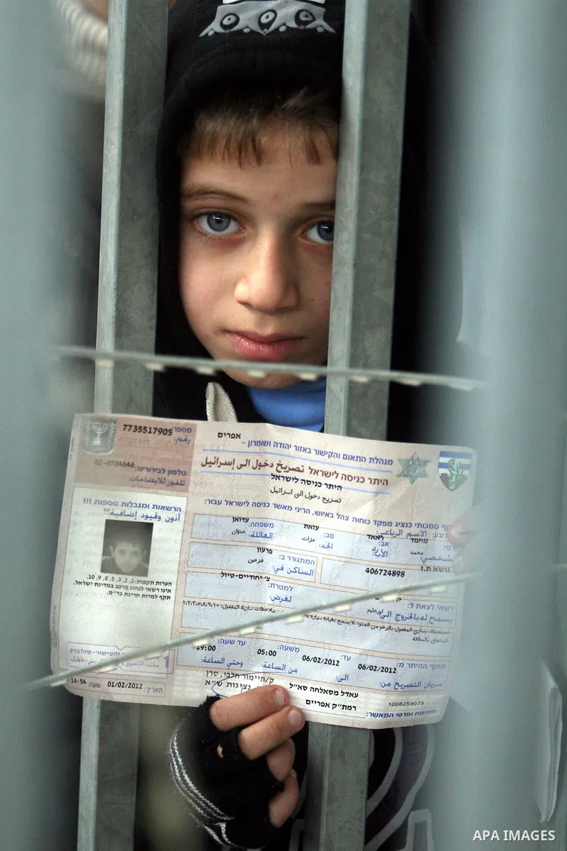 A Palestinian boy holds his permit to enter Israel as he waits at the Qalandia checkpoint between the West Bank city of Ramallah and Jerusalem, Monday, Feb. 6, 2012. Photo by Issam Rimawi