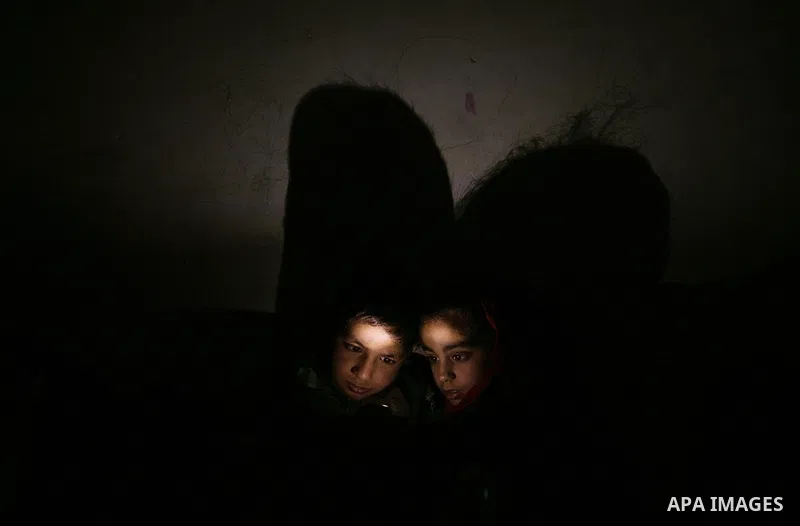 The display light of a mobile phone illuminates two Palestinian children playing games on the device at their familiy's home during an electricity power cut in the Jabaliya refugee refugee Gaza Strip, 07 February 2012. E...