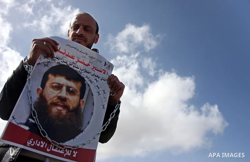 Palestinian protesters hold a placard that reads in Arabic "Khodr Adan our dignity is also more precious than food" during a demonstration outside the Israeli Ofer military prison, near the West Bank town of Betunia, on...