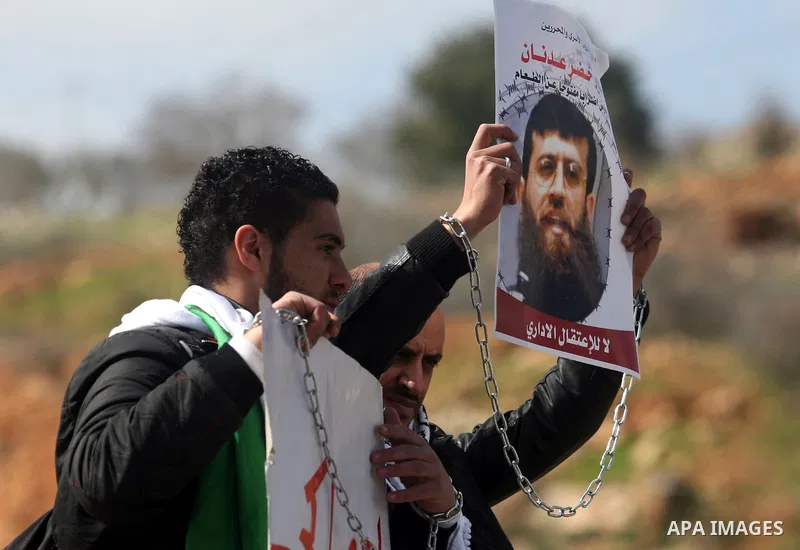 Palestinian protesters hold a placard that reads in Arabic "Khodr Adan our dignity is also more precious than food" during a demonstration outside the Israeli Ofer military prison, near the West Bank town of Betunia, on...