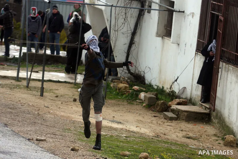 A Palestinian protester hurls stone at Israeli troops during a demonstration against the expansion of the nearby Jewish settlement of Halamish in the West Bank village of Nabi Saleh near Ramallah, Friday, Feb. 10, 2012....