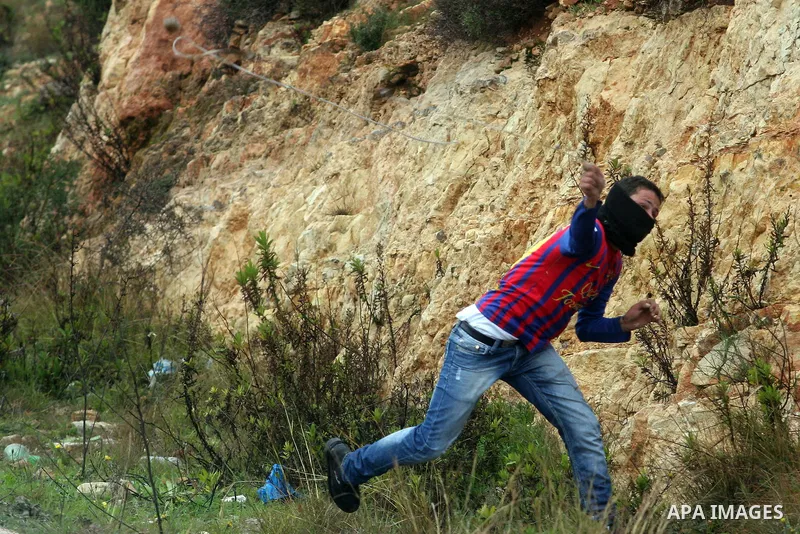 A Palestinian protester hurls stone at Israeli troops during a demonstration against the expansion of the nearby Jewish settlement of Halamish in the West Bank village of Nabi Saleh near Ramallah, Friday, Feb. 10, 2012....