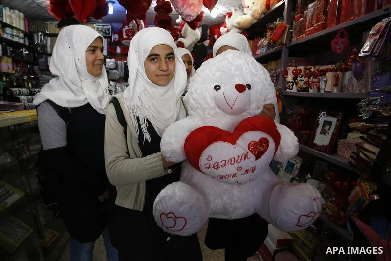 Palestinian girls are buying the hearts of love in the shop as they pass a display of hearts to commemorate Valentine's Day adorned with sayings about love, in Rafah, southern Gaza Strip on February 13, 2012. Valentine's...