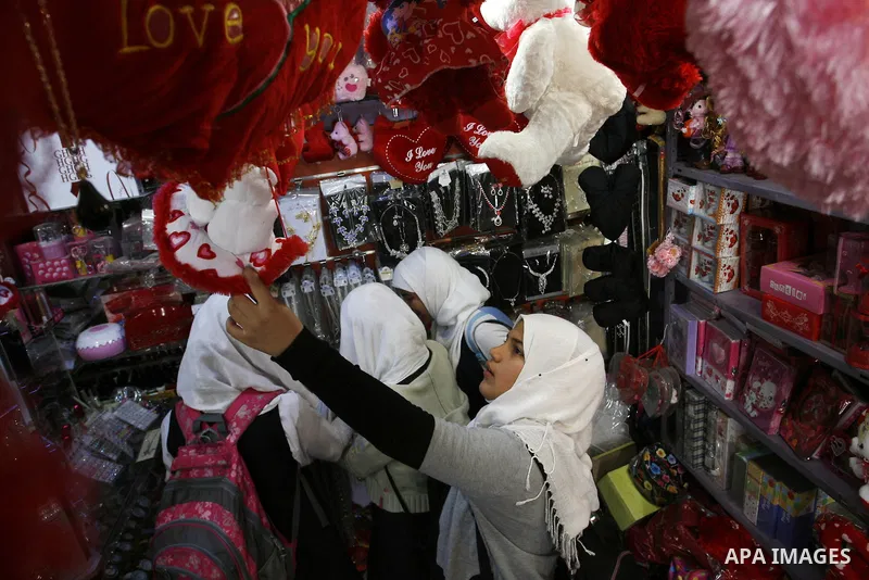 Palestinian girls are buying the hearts of love in the shop as they pass a display of hearts to commemorate Valentine's Day adorned with sayings about love, in Rafah, southern Gaza Strip on February 13, 2012. Valentine's...