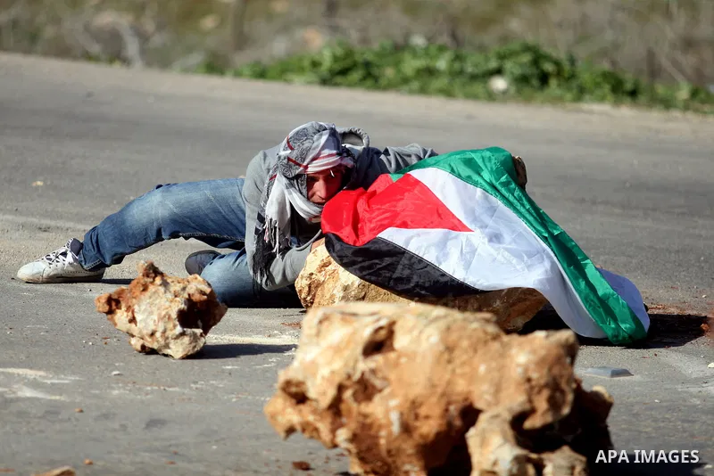 A Palestinian protester takes cover during clashes with Israeli security forces, partially visible in background, outside the Ofer military prison near the West Bank city of Ramallah, Monday, Feb. 13, 2012. Clashes betwe...