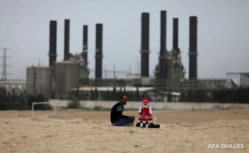 A Palestinian man with his baby sits in front of the power plant that generates electricity in Al-Nusirat in the central Gaza Strip, 14 February 2012. The Gaza Energy Authority said that the sole remaining power plant in...