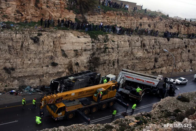 Israeli and Palestinian rescue workers stand with onlookers at the scene of an accident near the Qalandiya checkpoint outside the West Bank city of Ramallah February 16, 2012. At least five Palestinian children were kill...