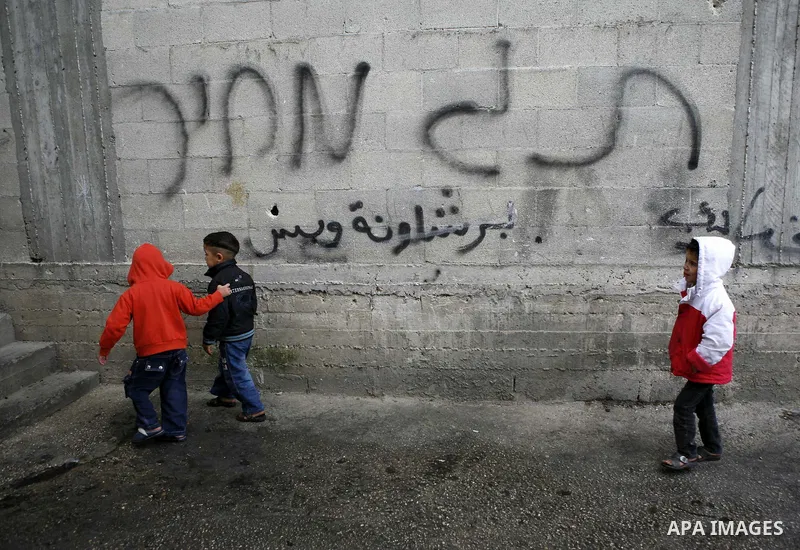 Palestinian boys walk by a wall showing the Hebrew written words 'price-tag', in the West Bank village of Nabi Elyas, near the West Bank city of Qalqilya , 16 Februray 2012. Right wing Israelis are suspected of having bu...