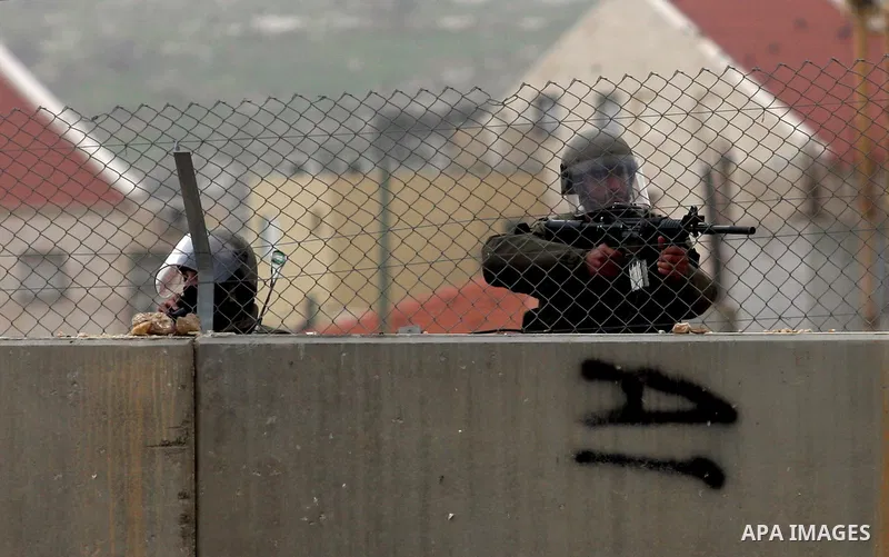 Israeli soldiers stand guard behind Israel's controversial separation barrier as posters of Palestinian prisoner Khader Adnan are placed by demonstrators on a barbed wire fence in the West Bank village of Bilin on Februa...