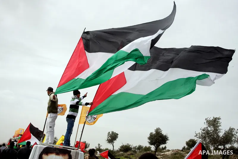 Palestinian activists hold Palestinian national flags in front of the separation barrier during a protest in the West Bank village of Billin, next to the Israeli settlement of Kereat Sefir, 17 February 2012, during a pro...