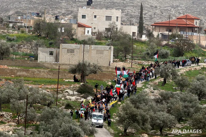 Palestinian activists hold Palestinian national flags in front of the separation barrier during a protest in the West Bank village of Billin, next to the Israeli settlement of Kereat Sefir, 17 February 2012, during a pro...