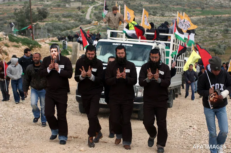 Palestinian protesters dressed as jailed Islamic Jihad leader Khader Adnan gesture as they take part in a weekly demonstration against the controversial Israeli barrier, in the West Bank village of Bilin near Ramallah Fe...