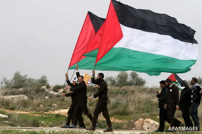 Palestinian activists hold Palestinian national flags in front of the separation barrier during a protest in the West Bank village of Billin, next to the Israeli settlement of Kereat Sefir, 17 February 2012, during a pro...