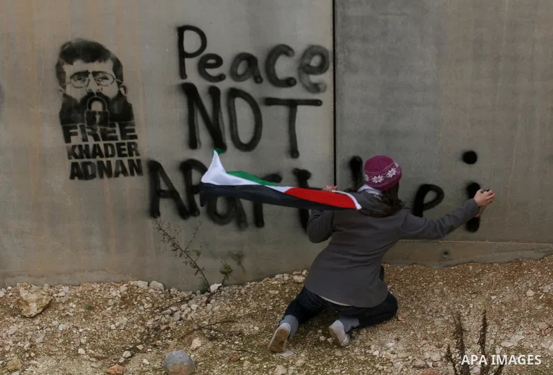 Palestinian activists spray paint a picture of the Palestinian prisoner Khader Adnan onto the separation barrier during a protest in the West Bank village of Billin, near the Israeli settlement of Kereat Sefir (backgroun...